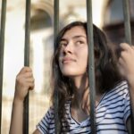 Sad isolated young woman looking away through fence with hope