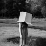 Faceless woman with cardboard box on head against pond