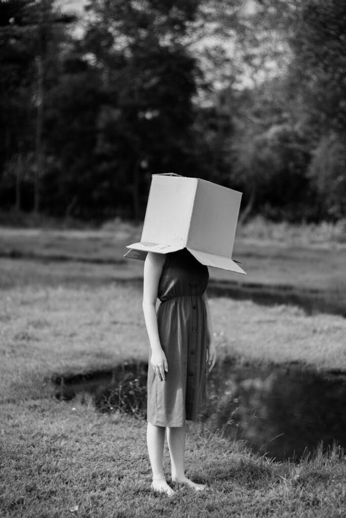 Faceless woman with cardboard box on head against pond